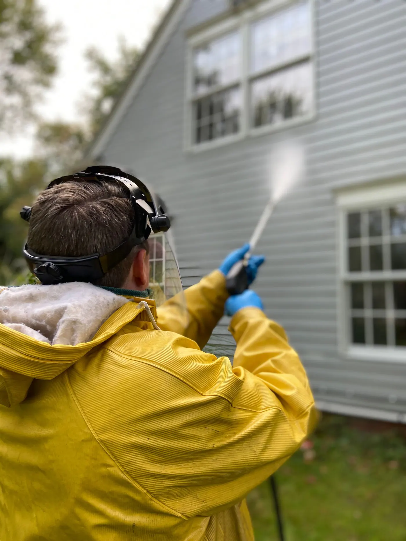 Person in a yellow jacket washing the weatherboard wall of a house