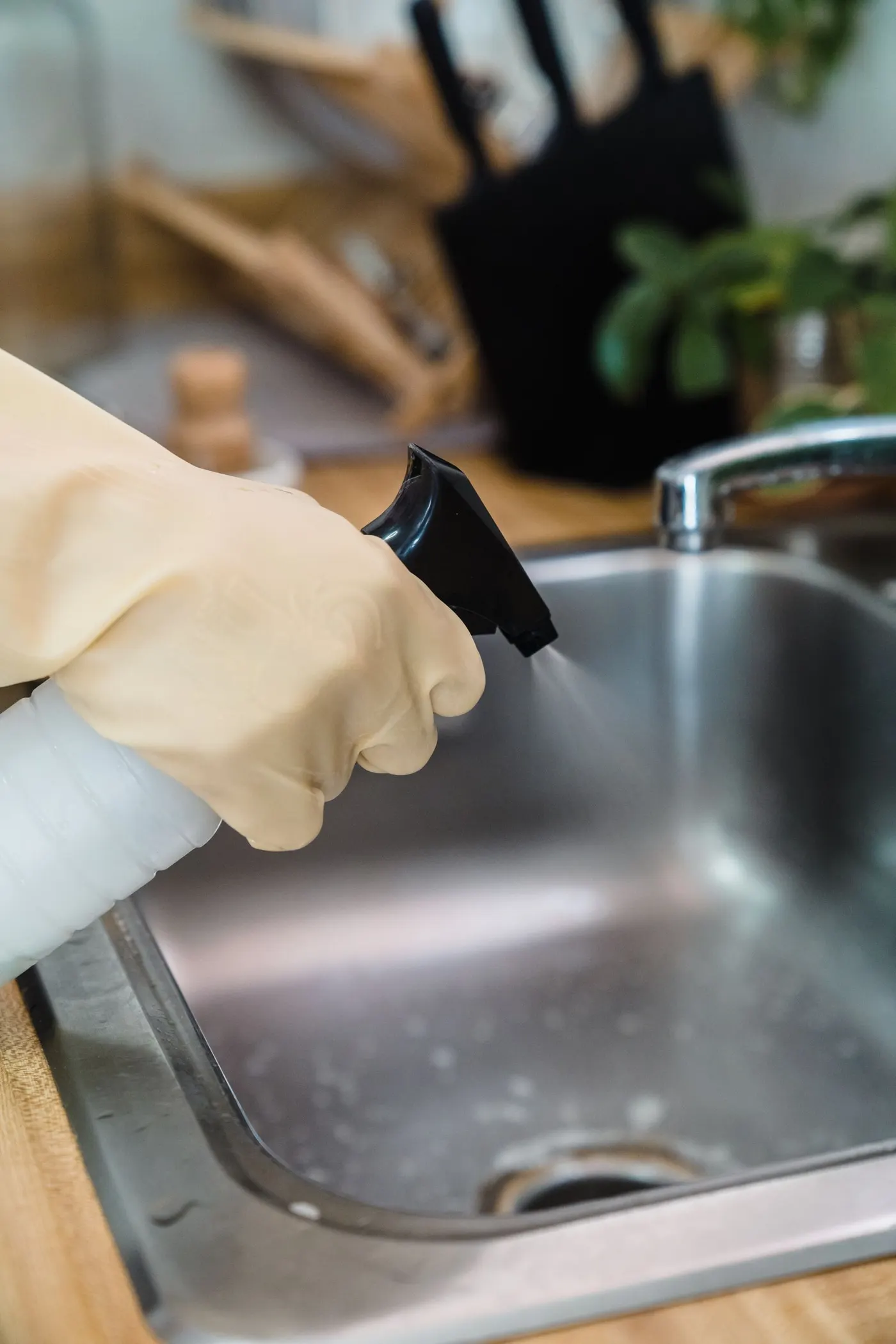 Gloved hand spraying cleaner into a stainless steel kitchen sink